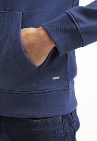 Sudadera azul marino con puños acanalados, bolsillo frontal y etiqueta metálica de marca, fabricada con un suave material de mezcla de algodón.