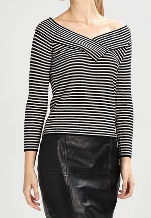 Haut à rayures noires et blanches à manches longues avec un design asymétrique décolleté, associé à une jupe crayon en cuir noir.