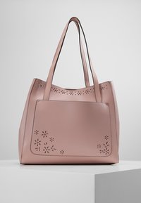 Różowa skórzana torba typu tote z kwiatowymi wycięciami. Posiada dwa długie uchwyty i usztywniony kształt. Gładka faktura i minimalistyczny styl.