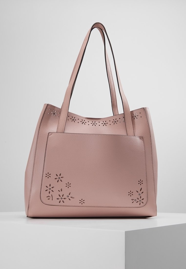 Różowa skórzana torba typu tote z kwiatowymi wycięciami. Posiada dwa długie uchwyty i usztywniony kształt. Gładka faktura i minimalistyczny styl.