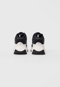 Black sneakers with a textured upper, padded collar, white midsole, and contrasting black rubber outsole. Features silver hardware on the heel.