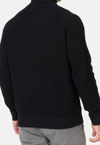 Pull en maille noire à col montant, motif texturé, poignets et ourlet côtelés. Vue de dos montrant une coupe décontractée et des manches raglan.