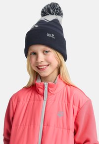 Marineblaue, gestrickte Mütze mit einem gemusterten Design und einem Quasten oben. Helles, pinkfarbenes, isoliertes Jacket mit grauen Akzenten und einem Logo auf der Brust.