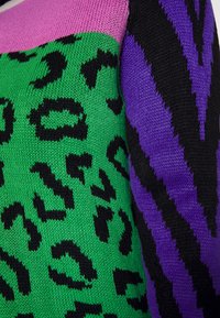Knit sweater featuring a green panel with black leopard spots, a purple zigzag stripe, and a pink upper section, with varied textures.