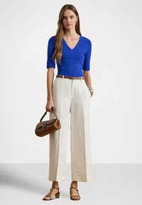 Modrý priliehavý top s krátkymi rukávmi, biele široké nohavice, hnedý kožený opasok a zladená kabelka. Kožené sandále s béžovým širokým podpätkom.