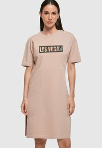 Rochie roz cu mânecă scurtă și decolteu rotund, având un grafic dreptunghiular "LAS VEGAS" în culori contrastante. Detaile sunt accentuate de fante laterale.