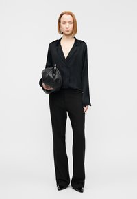 Μαύρο σατέν μπλούζα με λαιμόκοψη V, σε συνδυασμό με ραμμένο μαύρο παντελόνι. Το άτομο κρατάει μια μαύρη στρογγυλεμένη τσάντα με ασημί λεπτομέρεια.