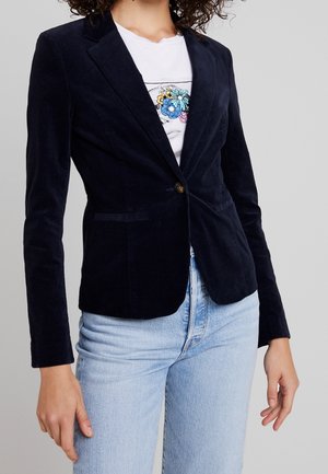 Marineblå kordfløyelsblazer med skräddarsydd passform, som har en knappstängning, slagkrage och två framfickor. Bärs över en t-shirt med tryck.