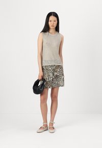 Beige strikket ermeløs topp med teksturdesign, kombinert med et skjørt i leopardmønster, svart håndveske og beige sandaler med stropp.