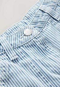 Un tissu à rayures bleu clair présente une texture subtile, avec un bouton en métal et des accents de couture au niveau de la taille et de la poche.