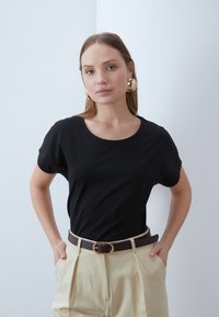 Svart kortärmad t-shirt med rund halsringning, tillsammans med högmidjade beige byxor och ett brunt bälte med en guldfärgade spänne.