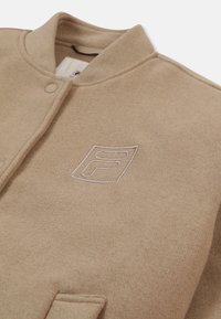 Beige Wollmischjacke mit runder Kragen, Druckknopfverschluss und Seitentaschen. Verfügt über ein gesticktes Logo in kontrastierender Farbe.