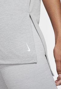 Primer plano de una persona que lleva leggings deportivos gris claro y una camiseta a juego, con una pequeña marca blanca de Nike cerca del dobladillo.