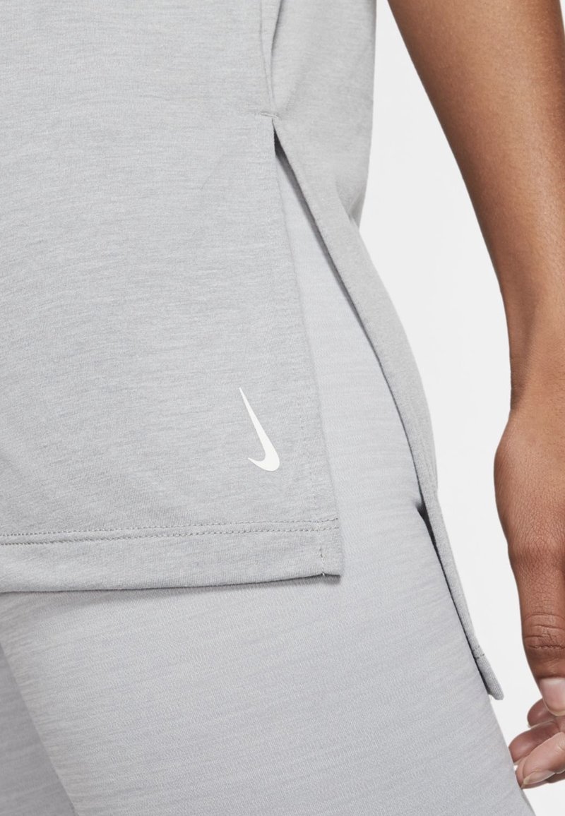 Primer plano de una persona que lleva leggings deportivos gris claro y una camiseta a juego, con una pequeña marca blanca de Nike cerca del dobladillo.