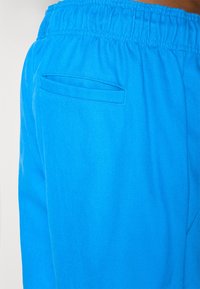 Μπλε υφασμάτινα σορτς με ελαστική μέση και μια μικρή, οριζόντια τσέπη στο πίσω μέρος, με λεία υφή και ζωντανό χρώμα.