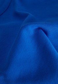 Deep blue fabric with a ribbed texture, showing folds and creases. The material appears smooth and stretchy, emphasizing its vibrant color.