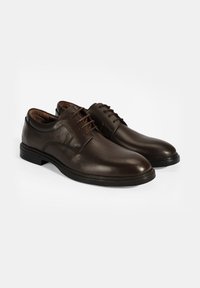Braune Lederanzugschuhe mit glatter Oberfläche, runder Zehenform und geprägten Details. Ausgestattet mit braunen Schnürsenkeln und einer schwarzen Gummisohle.