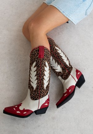 Knee-high western boots with white leather, leopard print, red accents, pointed toe, and cut-out detailing on the shaft and toe.