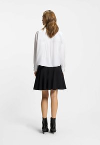 White blouse with long sleeves and a back pleat, paired with a black pleated skirt and black ankle boots with a zip. Smooth fabric texture.