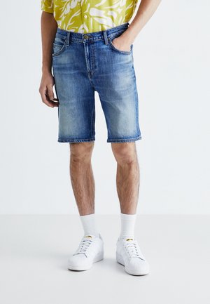 Denimshorts i ljusblått med en lätt sliten finish, med framfickor och uppvikt fåll, parat med vita sneakers och strumpor.