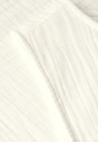 Vitt bomullstyg med en texturerad yta, med subtila veck och en slät kant. Designen är minimalistisk och enkel.