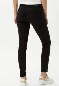 Zwarte spijkerbroek met een aansluitend model, elastisch materiaal, achterzakken en een gladde textuur, gecombineerd met witte en beige sneakers.