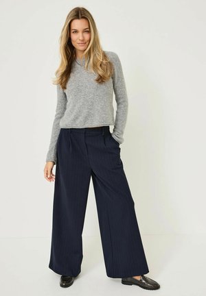 Un pull en tricot gris et un pantalon large à rayures marine. Texture lisse avec une coupe décontractée. Mocassins noirs, détails matériels minimaux.
