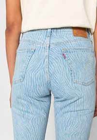 Ljusblå denimjeans med ett vågigt randigt mönster, försedd med bakfickor och en läderetikett vid midjan.