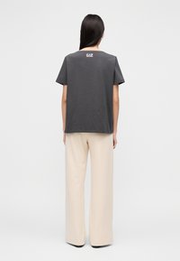 Szary bawełniany T-shirt z krótkimi rękawami, z małym białym logo z tyłu. W połączeniu z kremowymi, szerokimi spodniami z wysokim stanem.