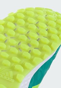 Semelle de chaussure de sport verte présentant un motif de traction texturé en jaune vif avec des formes hexagonales pour l'adhérence et la stabilité.