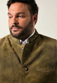Chaqueta corta de ante verde oliva con un cuello ajustado y costuras decorativas. Presenta un bolsillo en el pecho y herrajes plateados para el cierre.
