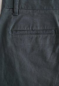 Grå stofbukser med en baglomme med et horisontalt spaltedesign og subtil tekstur, der har et skræddersyet og struktureret udseende.