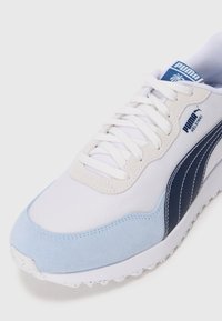 Sneaker bianca e azzurra chiara con punta in suede, tomaia in rete e strisce laterali blu navy con il marchio "PUMA HELSINKI" sulla linguetta.
