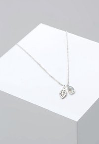 Collier chaîne en argent avec deux pendentifs : un en forme de feuille creuse et un ovale avec une pierre bleue irisée.