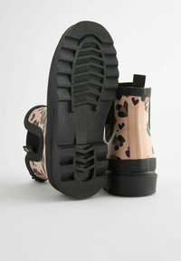 Bottes en caoutchouc à imprimé cœurs noirs sur un fond rose clair, avec une semelle noire texturée et une languette pour un enfilage facile.