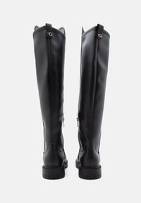 Botas de couro pretas até ao joelho com acabamento liso, fechos laterais e costura reforçada, apresentando uma sola com a marca e uma alça na parte de trás.