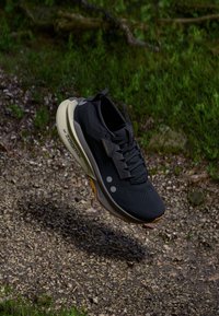 Black running shoe with breathable mesh upper, reflective accents, and a cushioned sole in light gray and orange. Lightweight design, textured fabric.