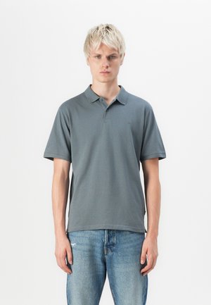 Polo shirt gris à manches courtes avec un col classique, en coton, un logo discret sur la poitrine et une coupe décontractée, associé à un jean bleu.