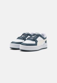 Sneakers wykonane ze skóry i materiału syntetycznego; białe z granatowymi akcentami, z perforacjami na nosku, płaskim sznurówką i grubą białą podeszwą.