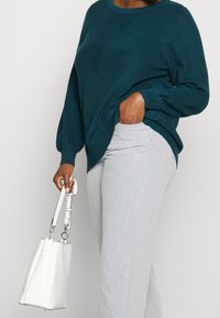 Morski sweter z dzianiny o prążkowanej fakturze i okrągłym dekolcie, zestawiony z jasnoszarymi spodniami i białą torbą typu bucket z srebrnymi dodatkami.