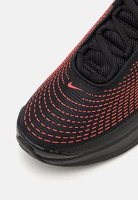 Čierna atletická obuv s červeným zakriveným prešívaním, vrchná časť z sieťoviny a čierna gumová podrážka. Obsahuje logo Nike na boku blízko šnúrok.