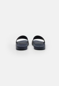 Sandali slip-on blu navy con una texture in gomma liscia, dotati di fasce larghe e suola piatta. Branding discreto sul lato.