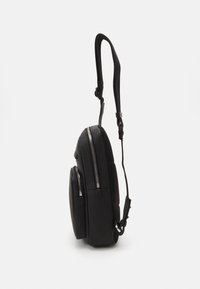 Sac à dos noir avec double fermeture éclair, tissu texturé, bandoulière ajustable et accents lisses, présentant une forme compacte et épurée.