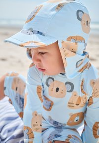 Light blue rash guard with bear and koala patterns, featuring a matching cap with flaps for sun protection and ribbed texture.