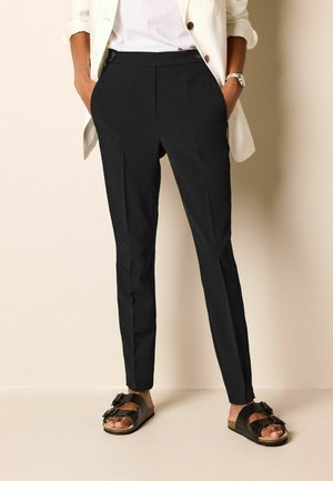 Black tailored trousers with a smooth texture, featuring a high waist, front pockets, and a slim fit. Paired with black sandals.