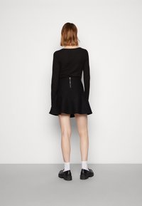 Top negro de manga larga combinado con una falda negra acampanada, con una cremallera en la parte posterior. El conjunto se complementa con zapatos negros y calcetines blancos.