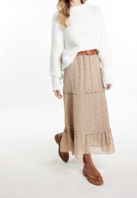 Pull blanc duveteux, jupe longue beige à fleurs avec volants, ceinture marron et bottines marron avec une semelle texturée.