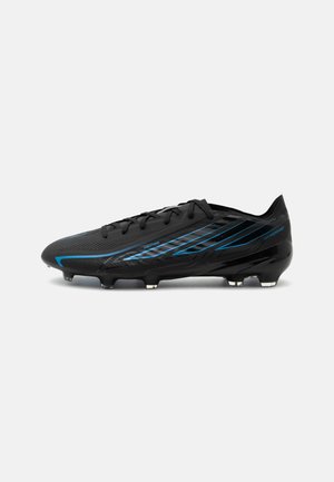 Schwarzer Fußballschuh mit blauen eckigen Streifen, abgerundeten Nocken an der Sohle und Schnürverschluss, von der Seite auf weißem Hintergrund gezeigt.