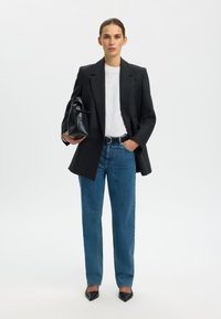 Hall hall villane bleiser valge T-särgi peal, kombineeritud siniste kõrge vöökohaga teksade ja mustade teravate kontsakingadega; käes must käekott.