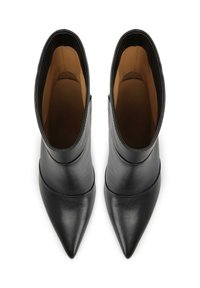Botines de cuero negro hasta el tobillo con punta afilada, diseño elegante y textura suave. Presentan un interior en color marrón claro que contrasta. Estilo minimalista.
